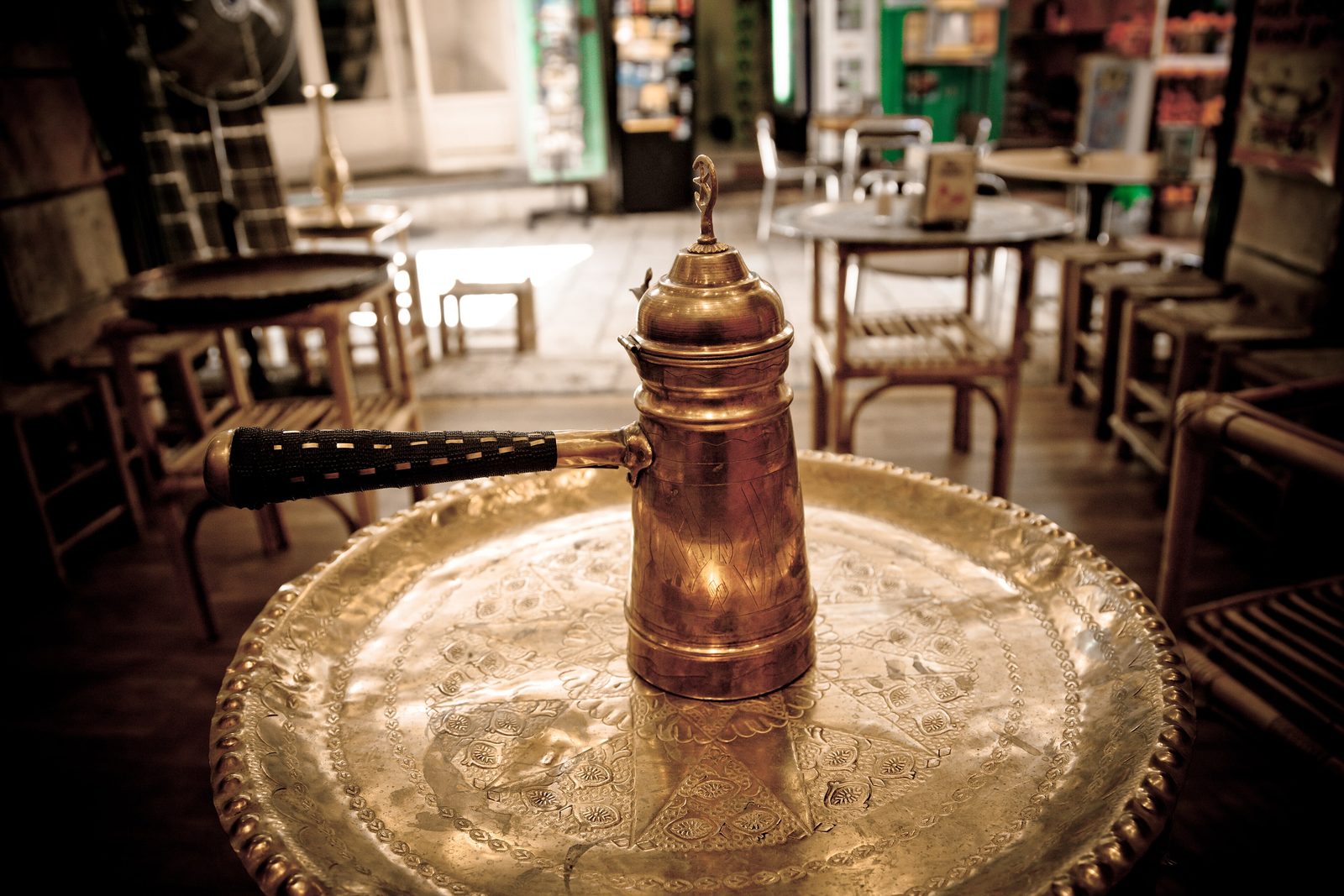 A traditional Turkish copper cezve coffee pot beside a small porcelain demitasse of strong black Turkish coffee, served on a small wooden tray with a piece of rose lokum on a separate saucer and a glass of water alongside