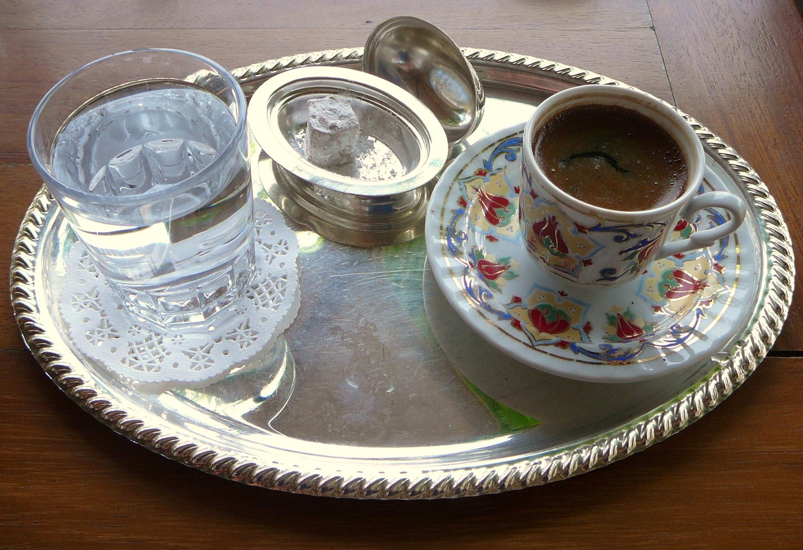 The traditional Turkish coffee service at a Bosphorus coffeehouse — a small porcelain cup of Türk kahvesi on a saucer, a piece of rose lokum and a tulip glass of water beside it