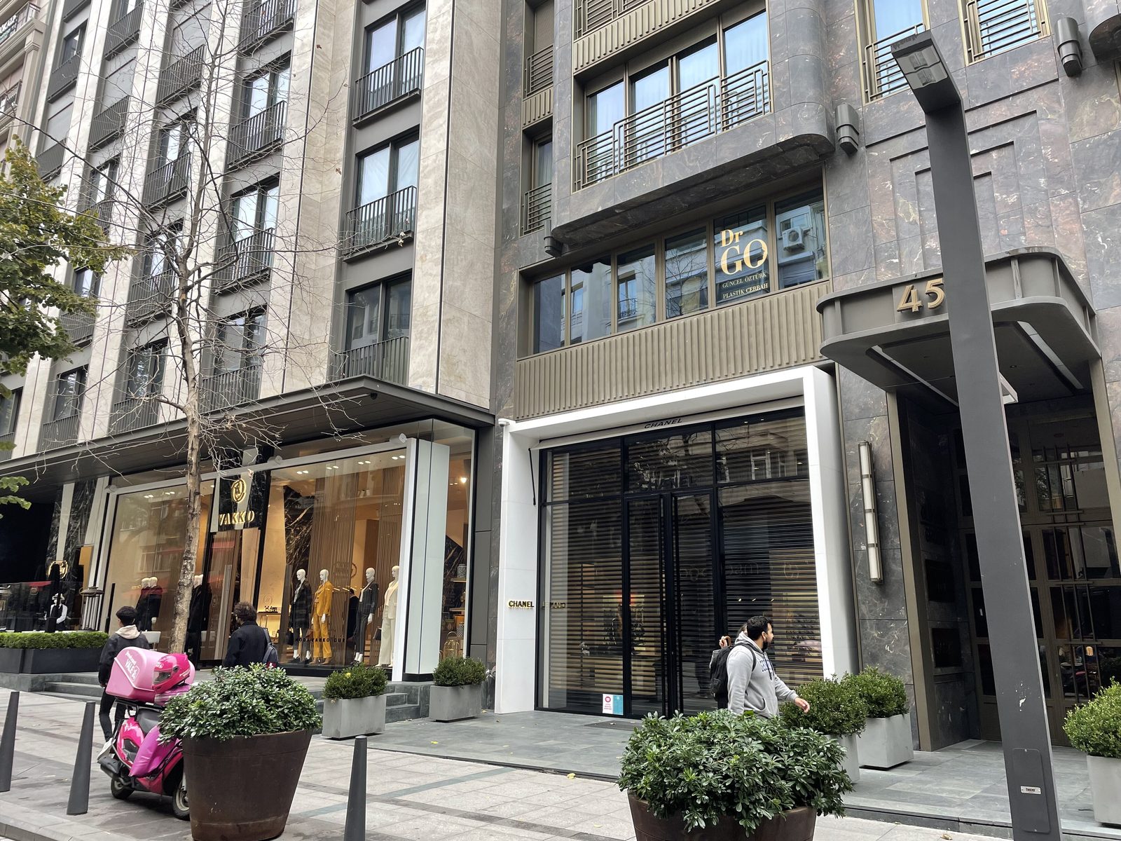 The Abdi İpekçi Caddesi boutique block in Nişantaşı — dressed-stone facades, designer storefronts including Vakko and Chanel, planted pavement trees and a few pedestrians on the cobbled walkway