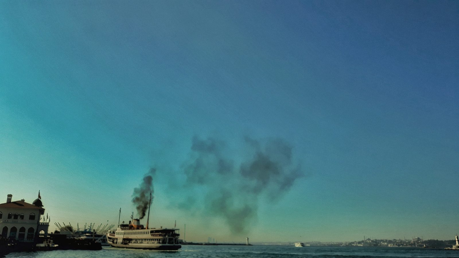 The Bosphorus strait seen from the Asian shore, a passenger ship crossing the open water with the Istanbul skyline low on the far bank